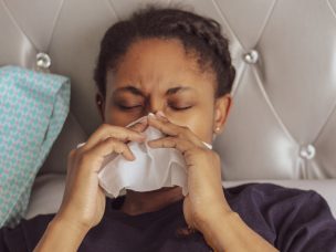 A young girl sick in bed blowing her nose and suffering from seasonal allergies
