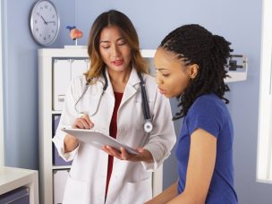 African American patient explaining issues to Asian doctor using tablet
