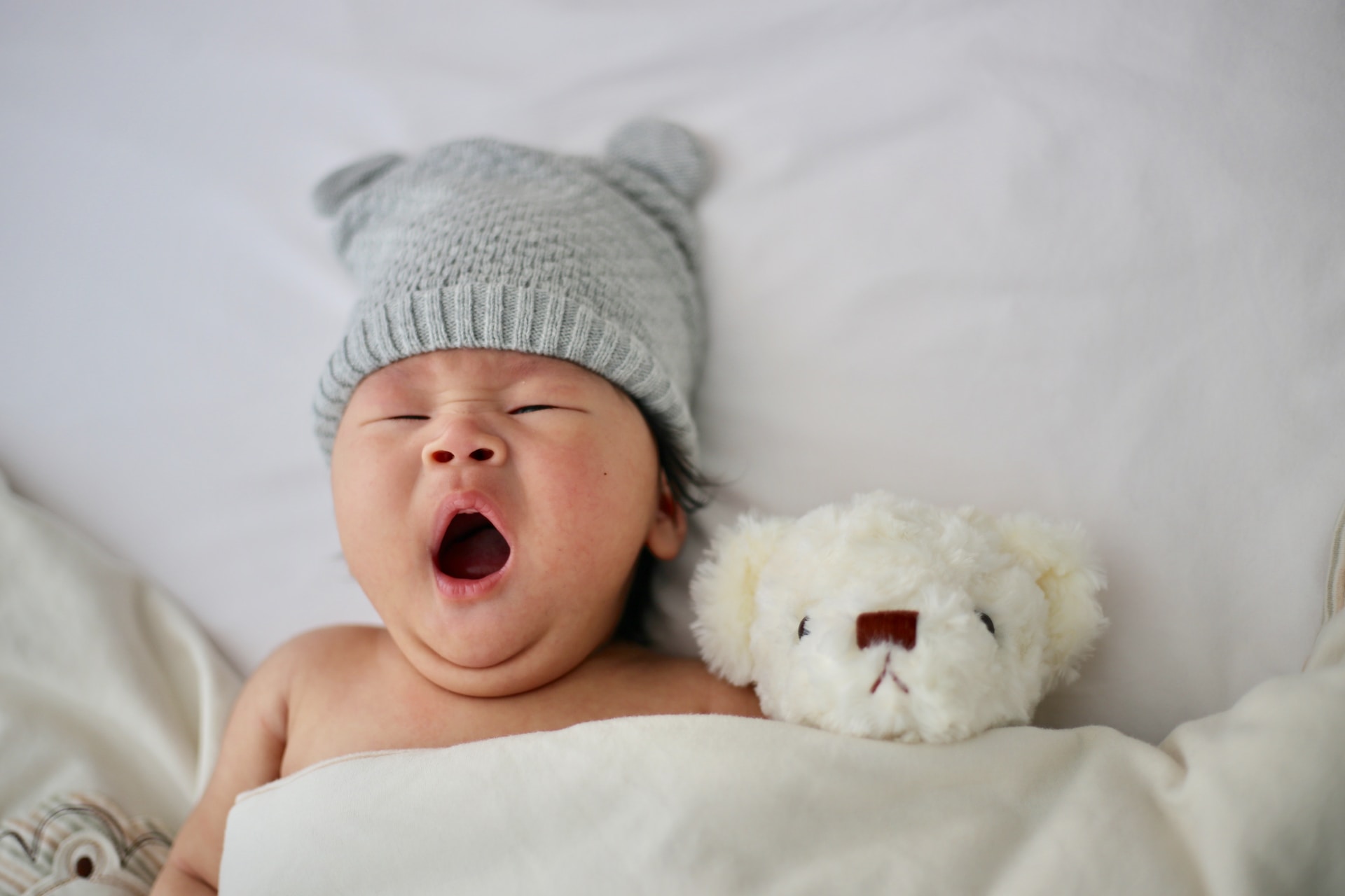 A baby with their mouth open laying with a bear toy
